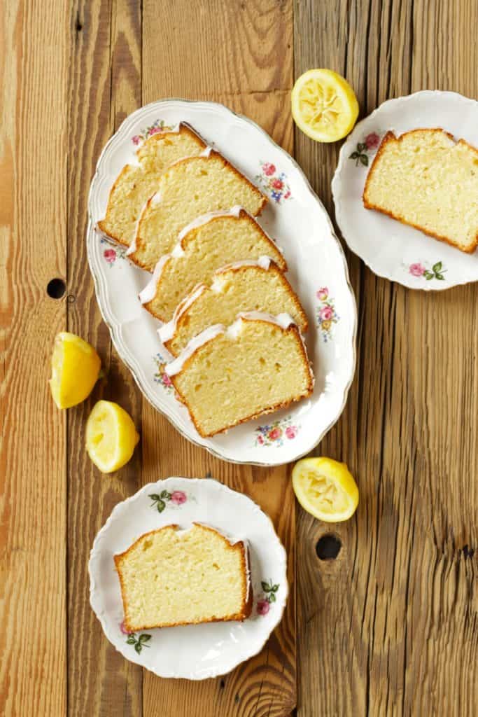 slices of lemon loaf cake on 3 white flowered plates on wooden surface viewed from above