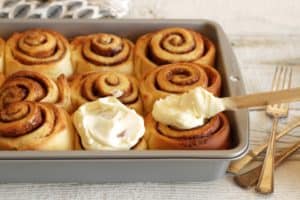 cinnamon rolls being frosted in pan