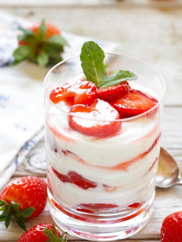 Klares Glas gefüllt mit weißer Topfencreme, geschichtet mit marinierten Erdbeeren