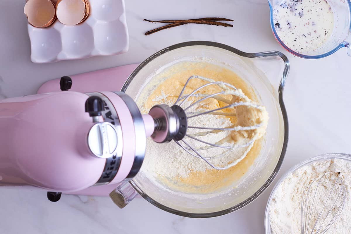 pink kitchen aid with glass bowl filled with vanilla cupcake batter sprinkled with flour